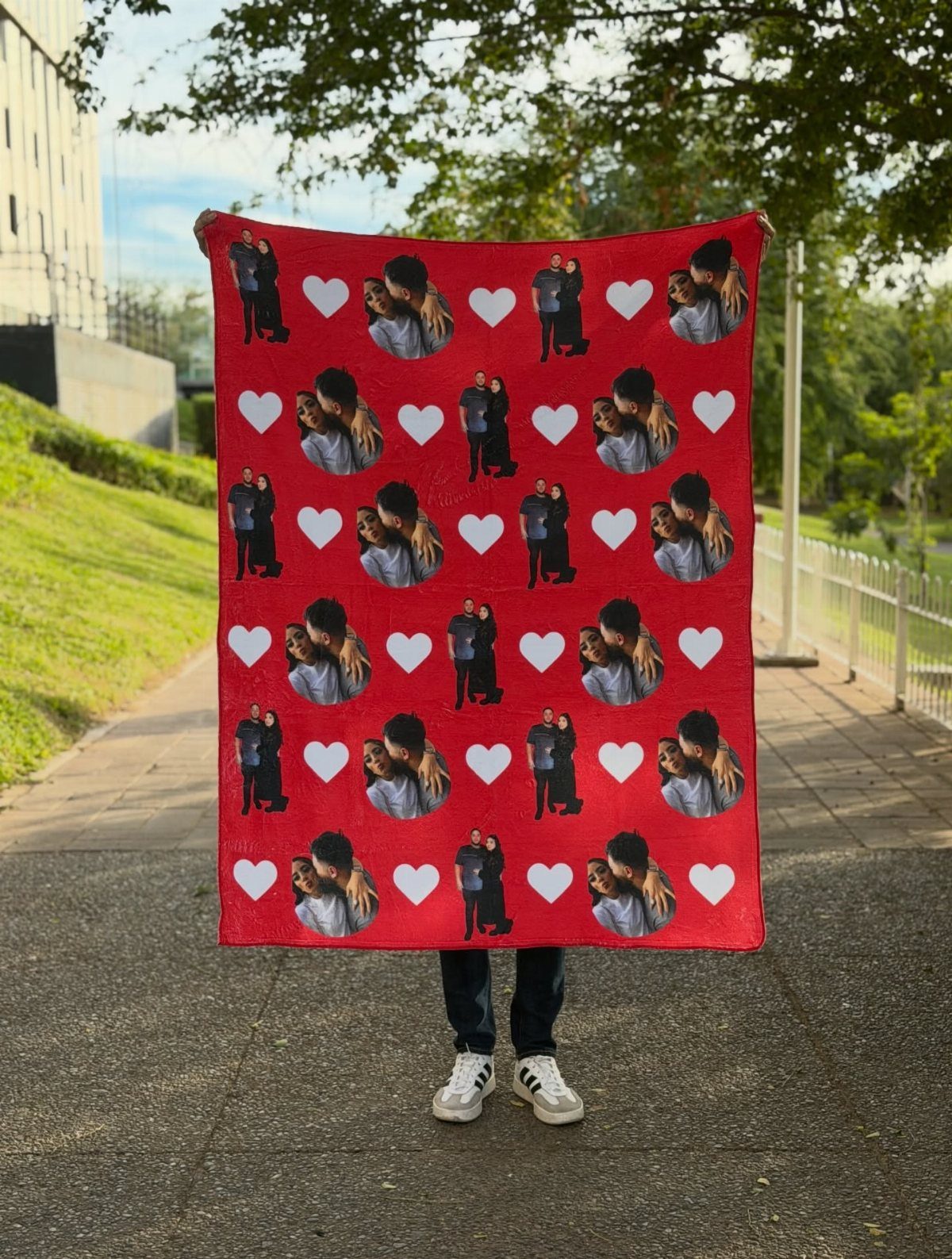 Red custom photo blanket with repeating couple pictures and white hearts held outdoors.