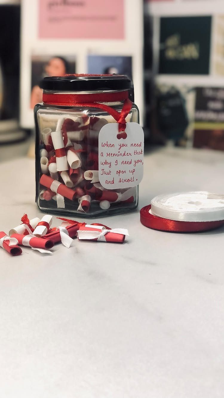 Glass jar filled with red and white rolled paper notes and a handwritten tag.