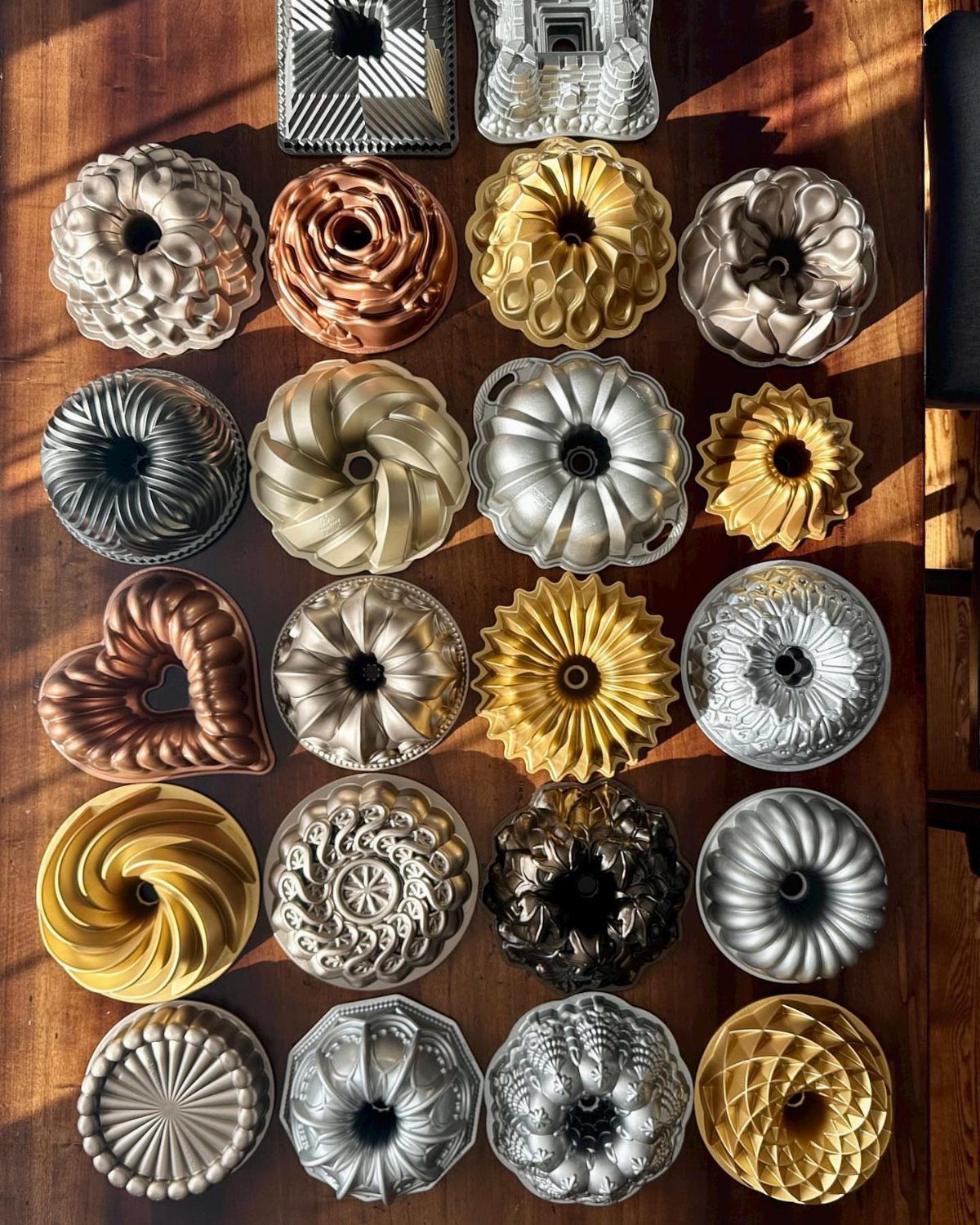 Various ornate metal Bundt cake pans arranged on a wooden tabletop.