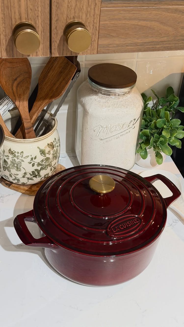 Red enameled Dutch oven on a white marble kitchen counter with cooking utensils.