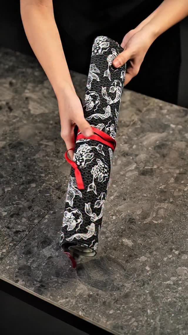 Hands holding a black and white floral fabric knife roll on marble countertop