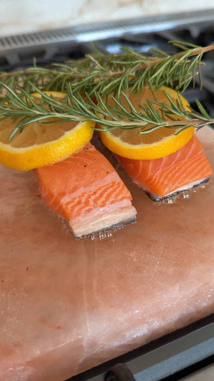 Salmon fillets with lemon and rosemary searing on a pink salt block.