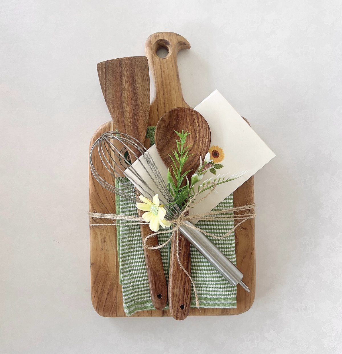 Wooden cutting board gift set with utensils, towel, and card tied with twine.