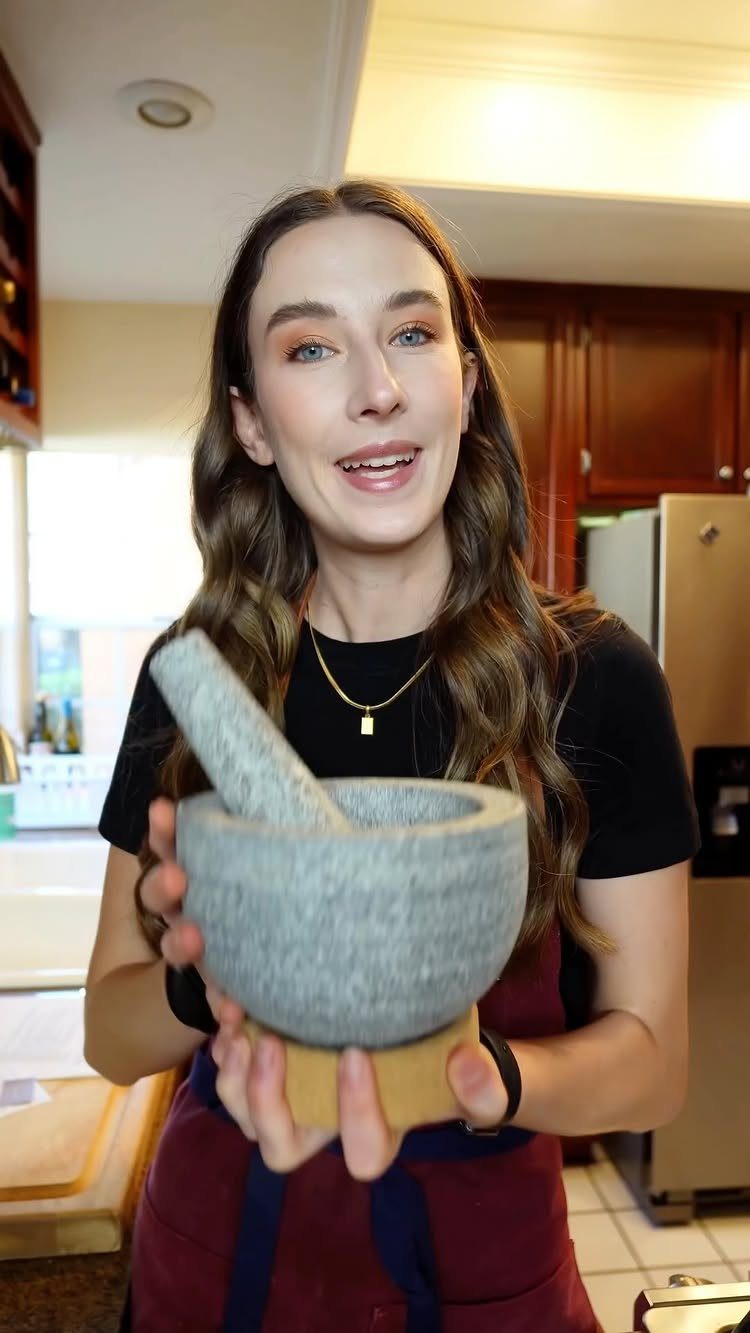 Woman holding a grey stone mortar and pestle set in a home kitchen.
