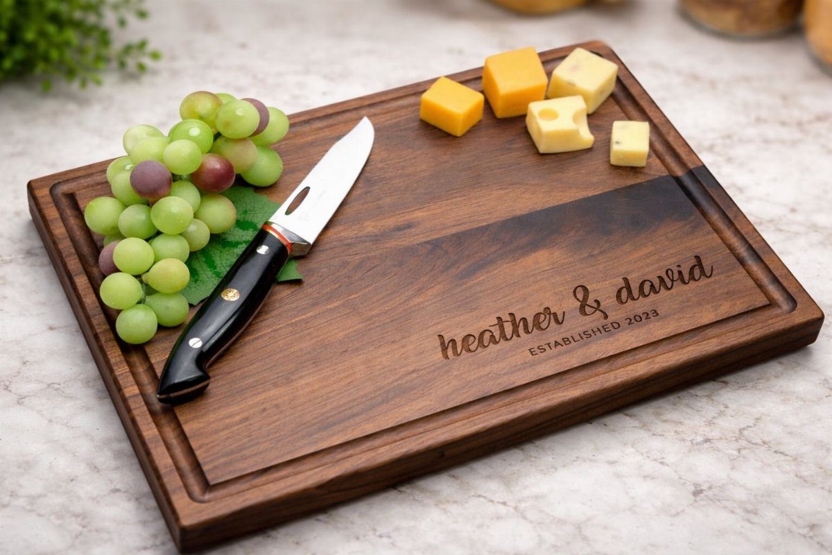 Engraved wooden cutting board with grapes, cheese cubes, and a small knife.