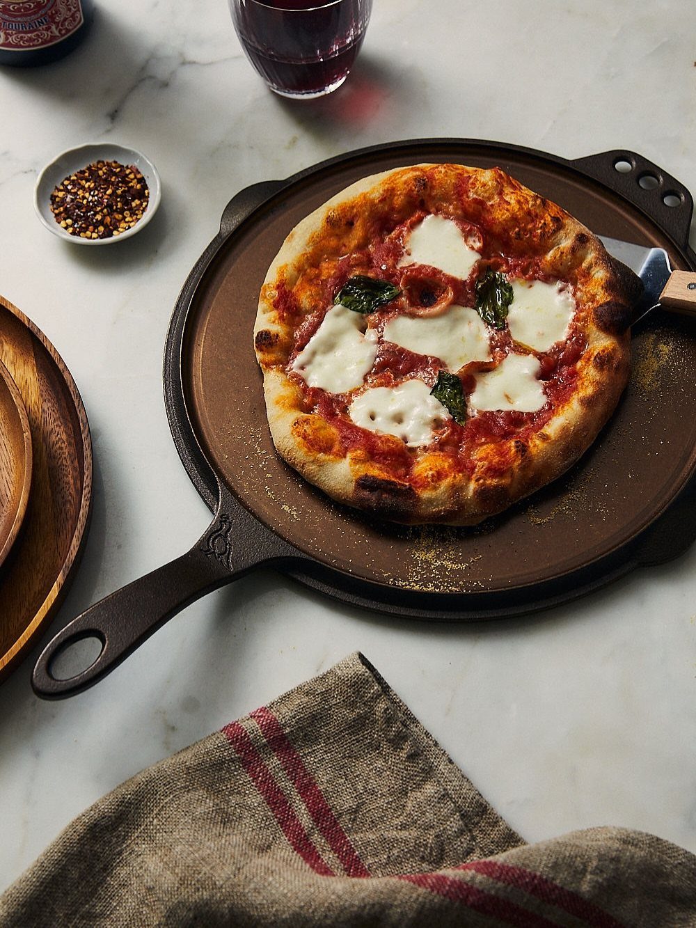 Margherita pizza on a cast iron pizza pan over a white marble surface.