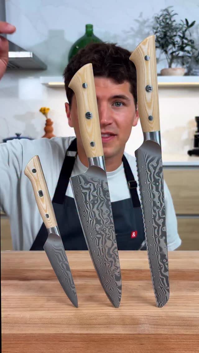 Three Damascus steel chef knives standing upright on a wooden cutting board.