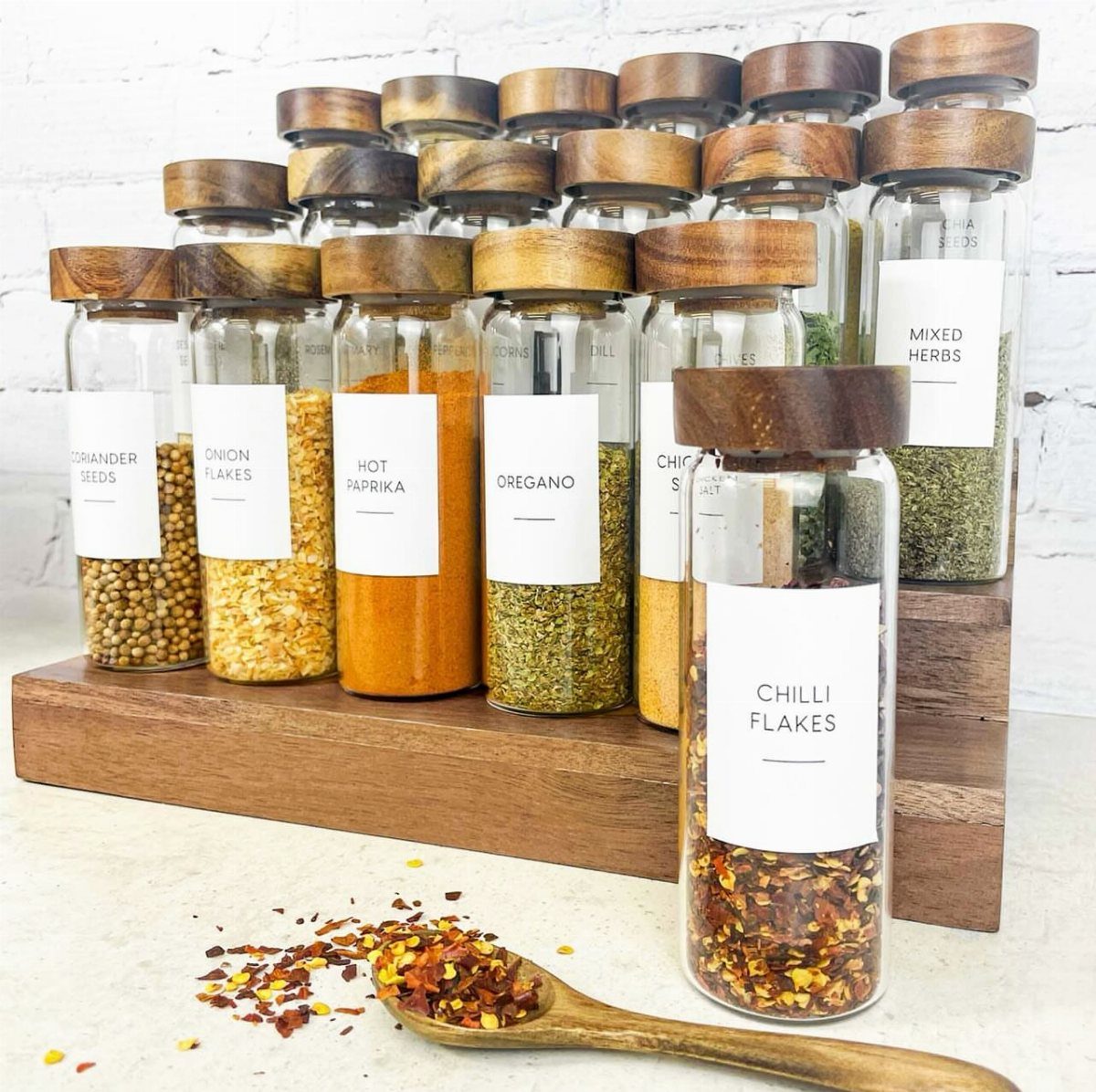 Glass spice jars with wooden lids on a rack with a wooden spoon.