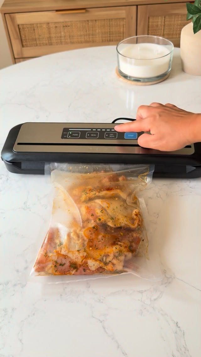 Vacuum sealer machine sealing a plastic bag of seasoned raw meat on marble.