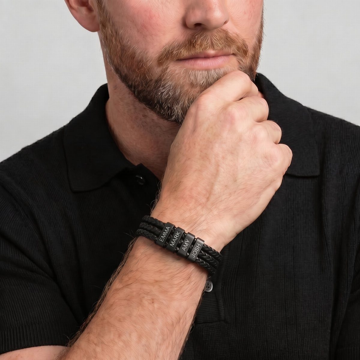 Man with a beard wearing a black braided leather bracelet and polo shirt.
