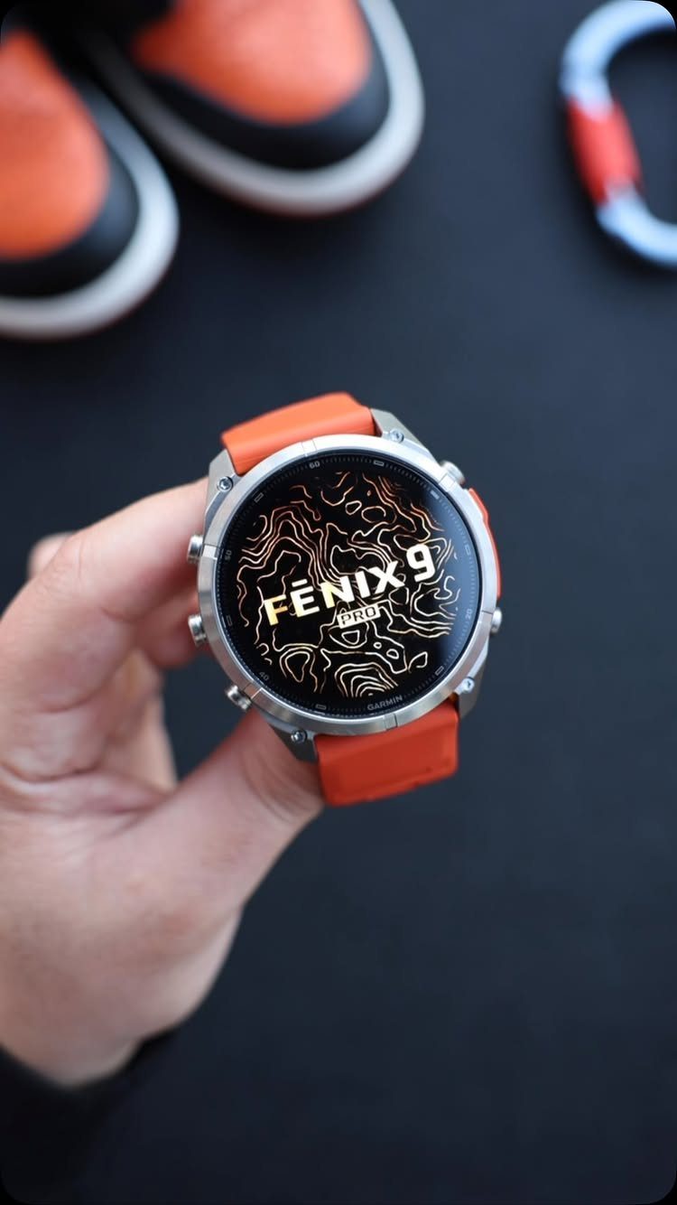 Silver smartwatch with orange strap held by a hand against dark background