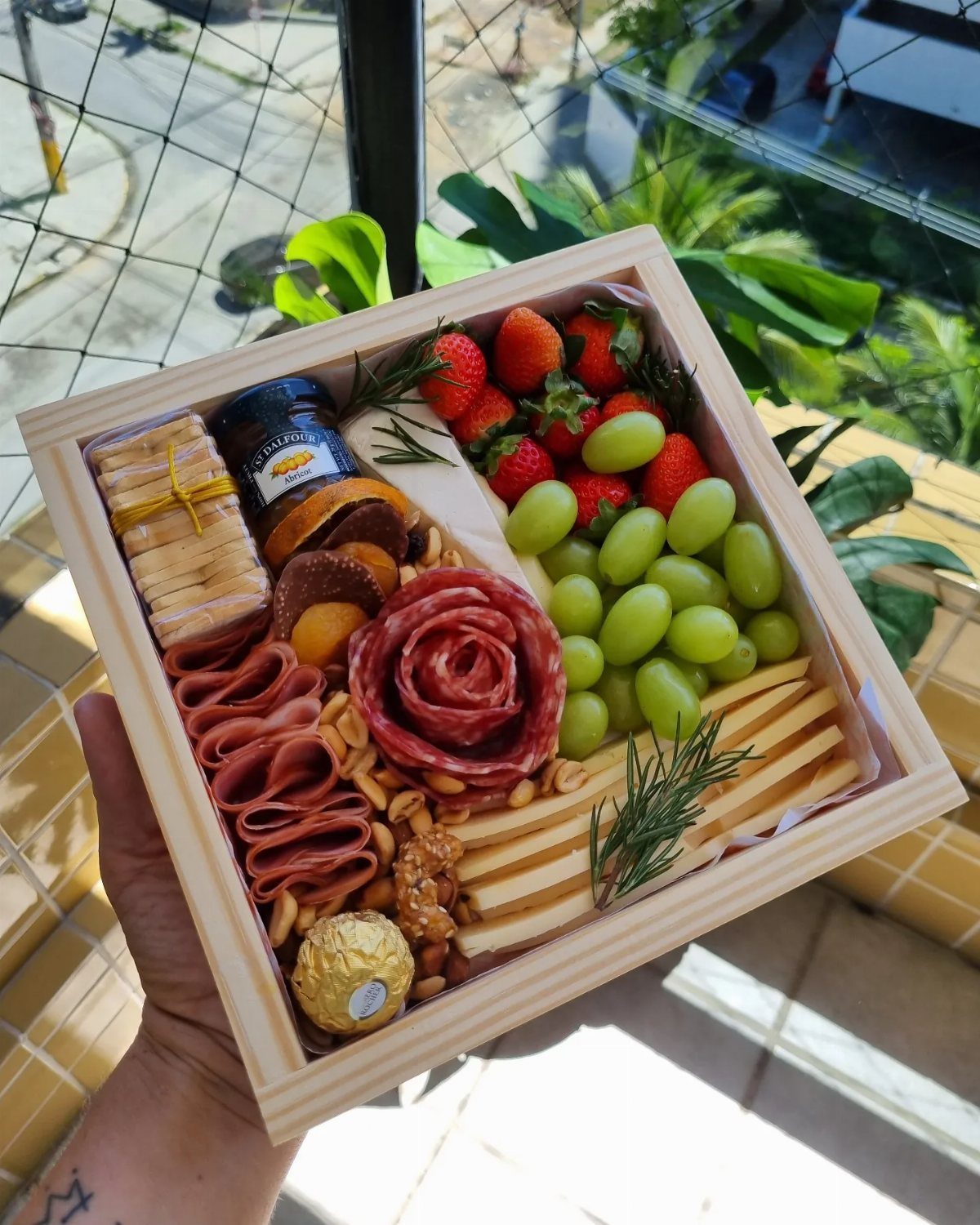 Wooden snack box filled with salami rose, grapes, strawberries, cheese, and crackers.