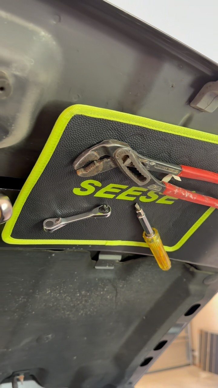 Tool organizer with pliers, wrench, and screwdriver attached to a car hood