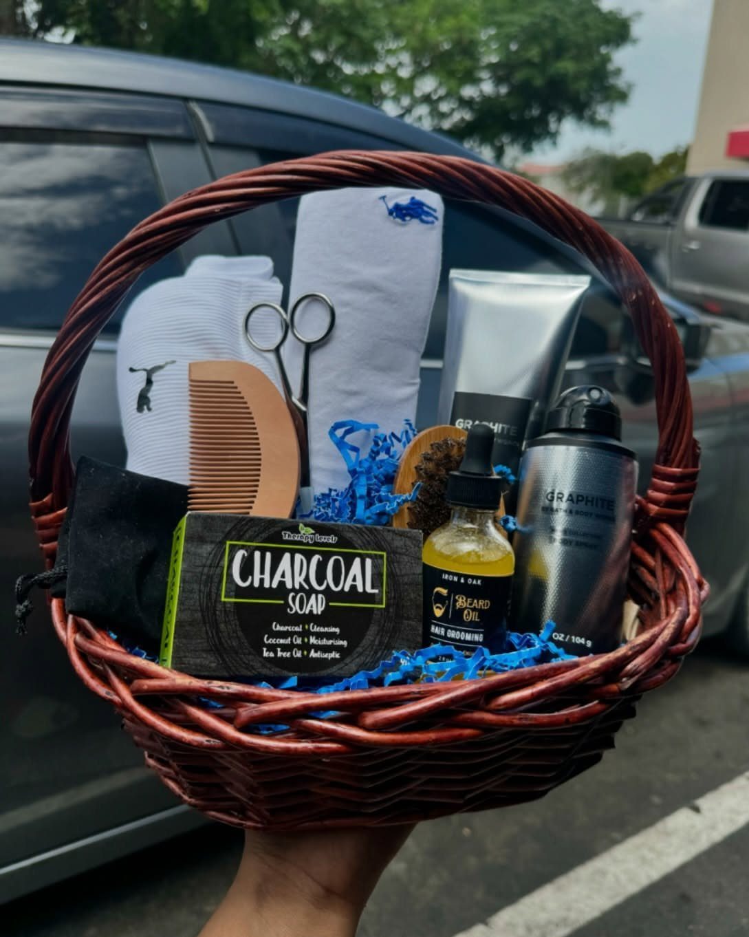 Grooming gift basket with beard oil, charcoal soap, comb, and white towels.