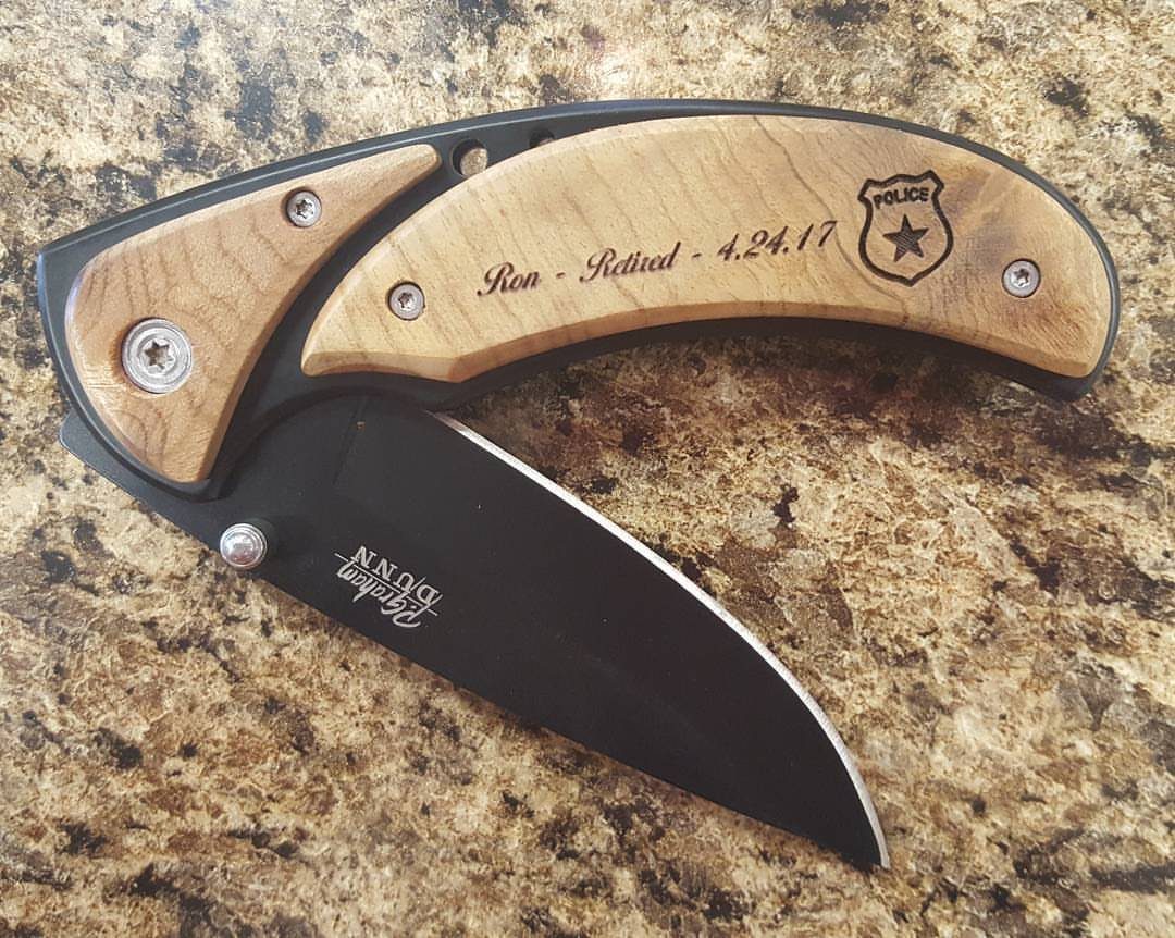 Open folding pocket knife with engraved wooden handle on a granite countertop