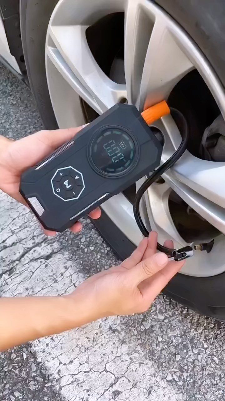 Portable air compressor inflating a silver car tire on a grey pavement.