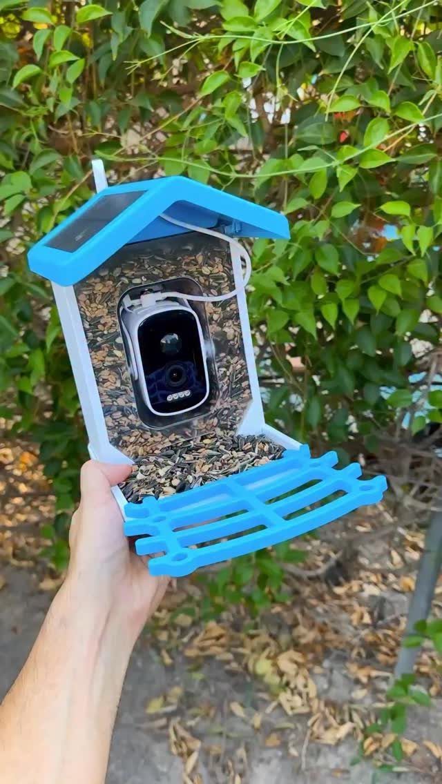 Smart bird feeder with built-in camera and solar panel held against green leaves