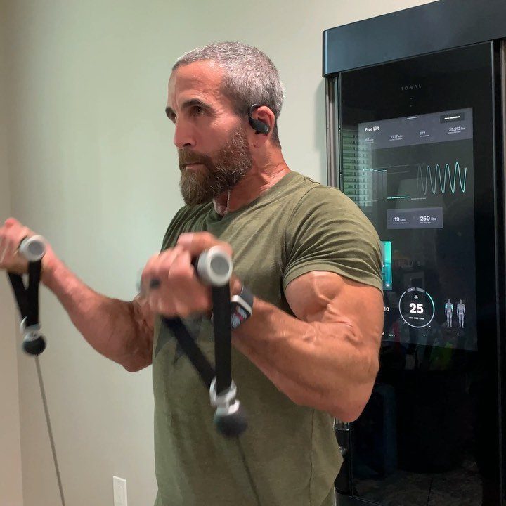 Muscular man with a beard exercising using a Tonal digital home gym machine.