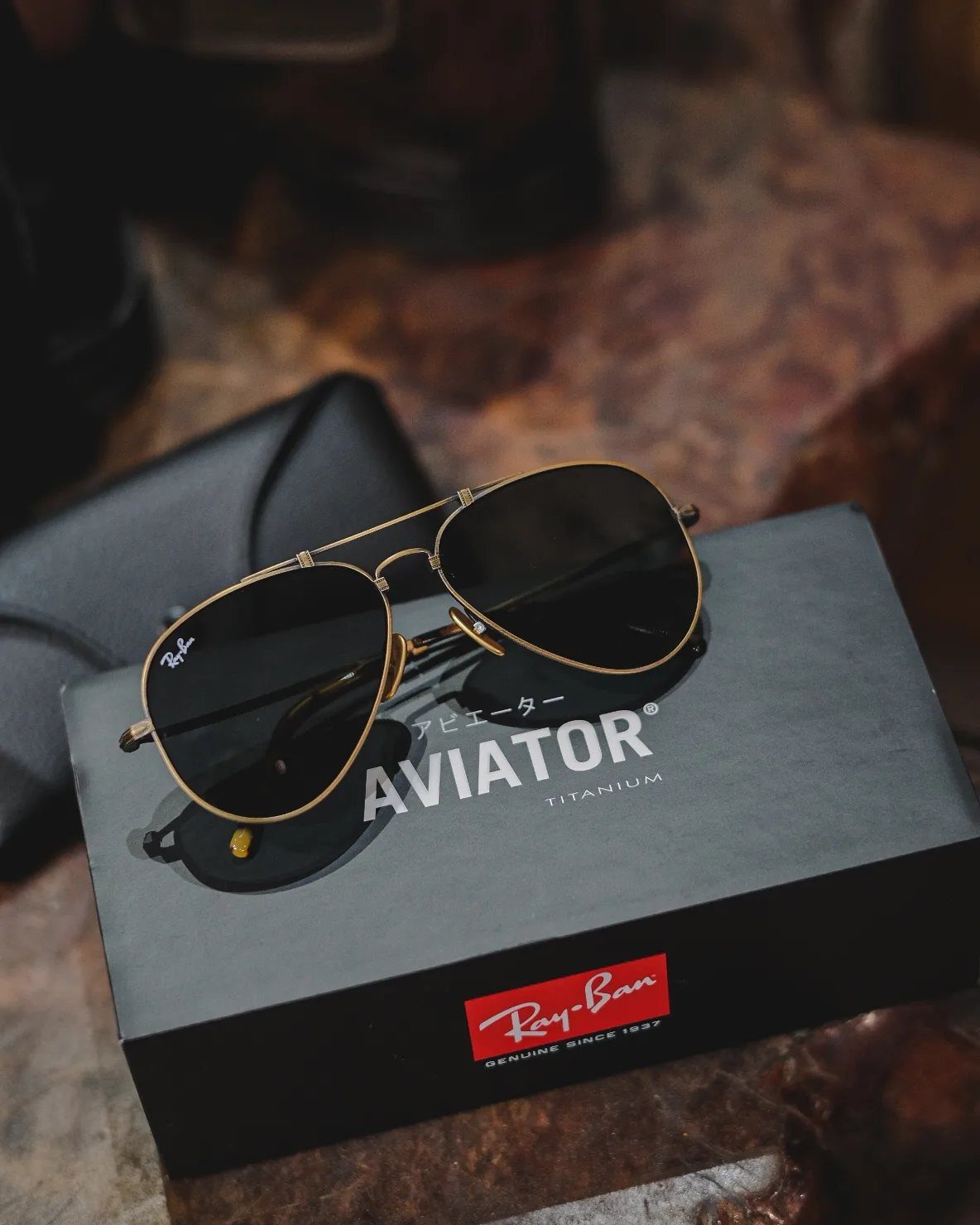 Gold aviator sunglasses resting on a black Ray-Ban branded box and case.