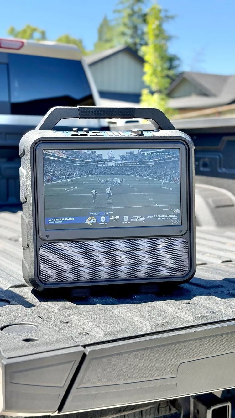 Portable screen displaying a football game on a pickup truck tailgate outdoors