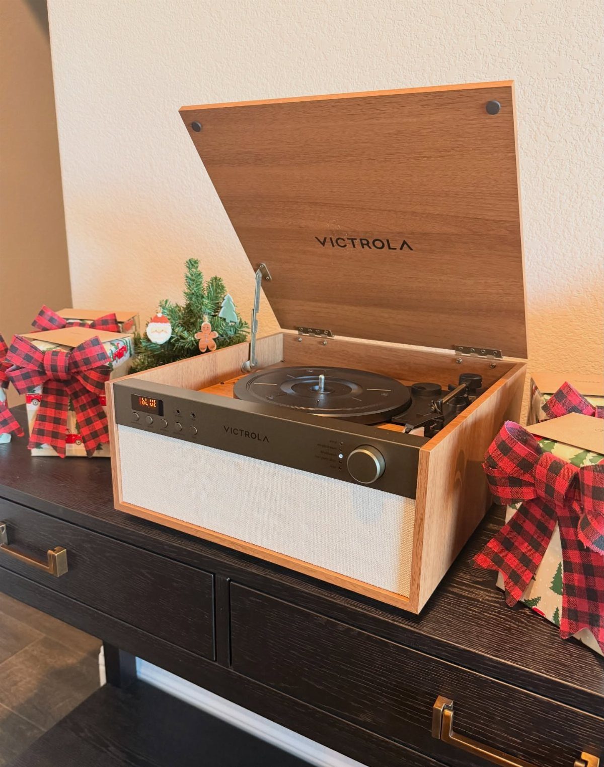 Victrola record player on a dresser surrounded by wrapped gifts with plaid bows