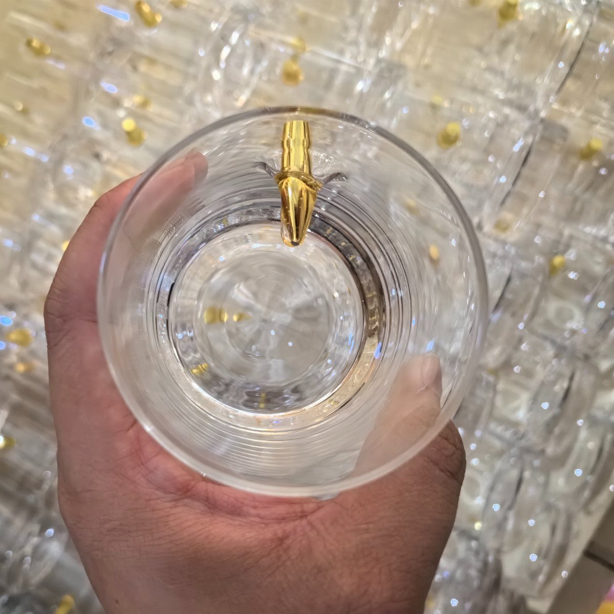 Clear glass held by a hand containing a gold bullet-shaped whiskey stone
