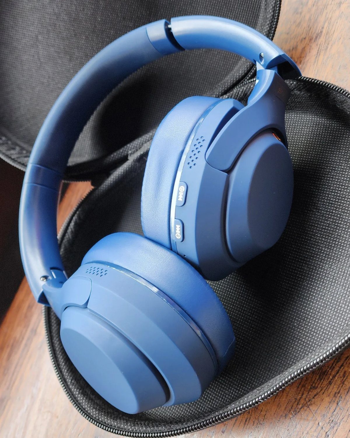 Blue wireless headphones resting inside a black protective carrying case on wood.