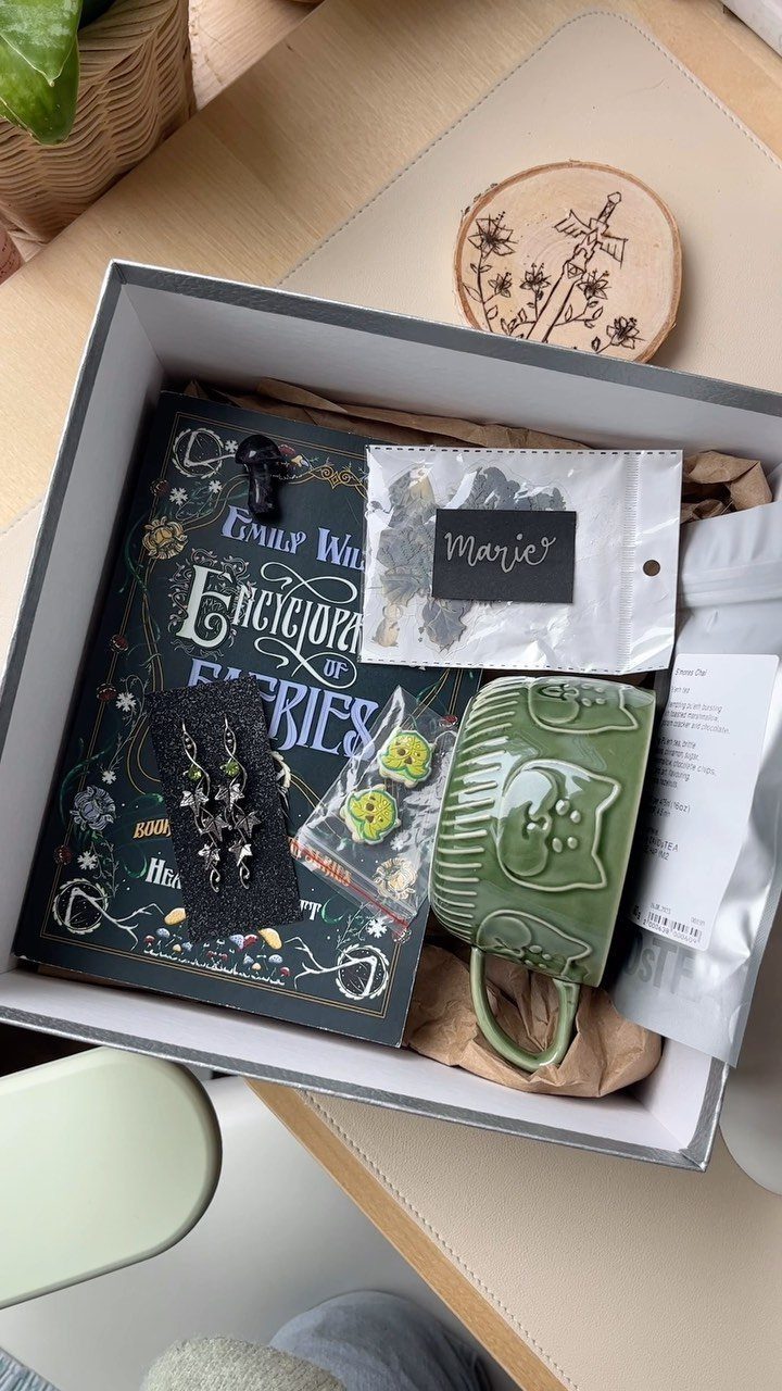 Gift box with a fairy encyclopedia book, green cat mug, and tea packet.