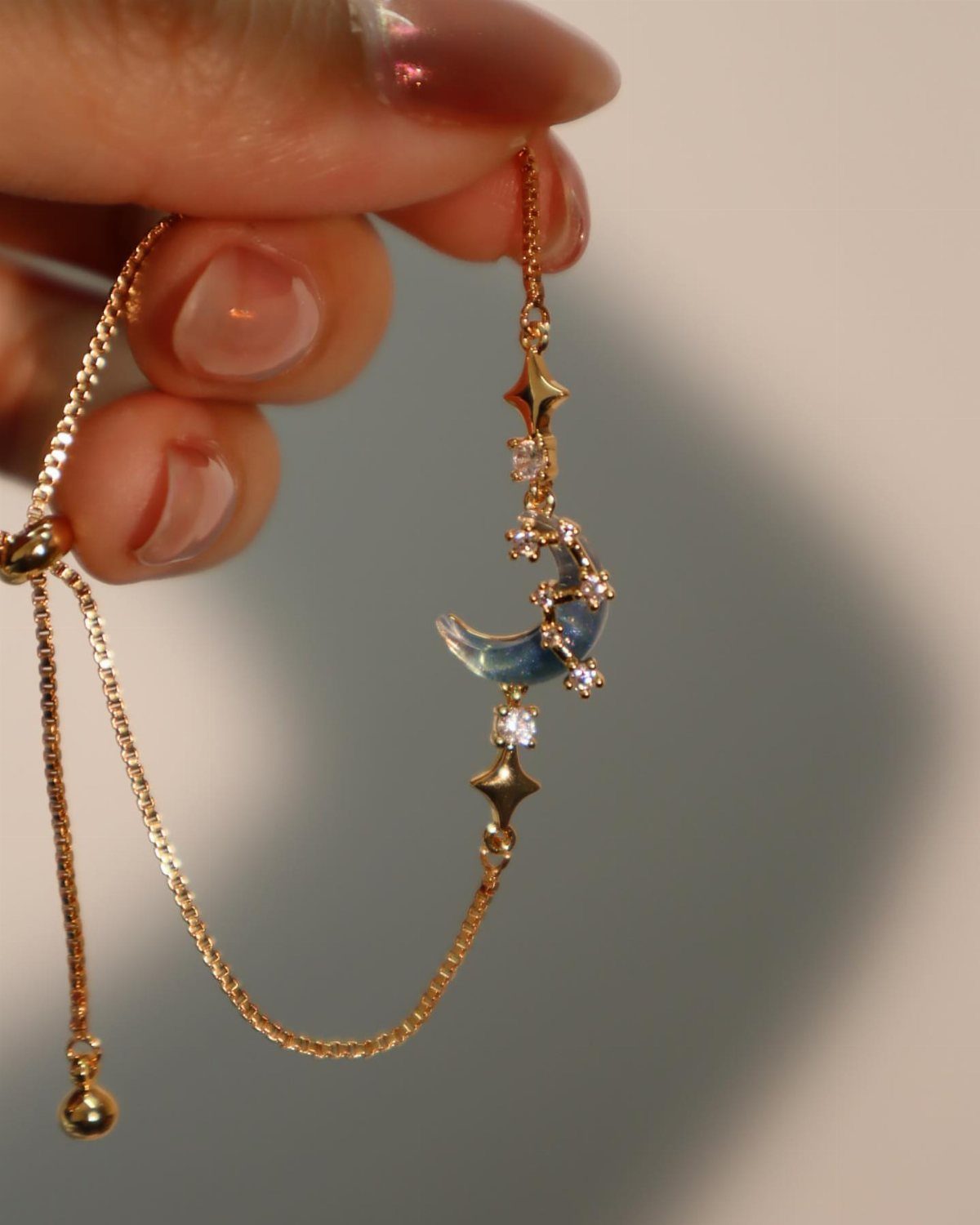 Gold chain bracelet with a blue crescent moon and star charms held by hand
