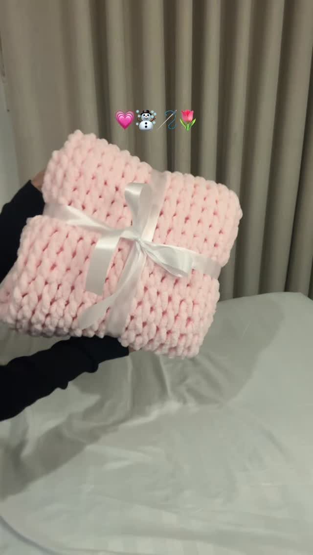 Chunky knit pink blanket tied with a white satin ribbon bow.