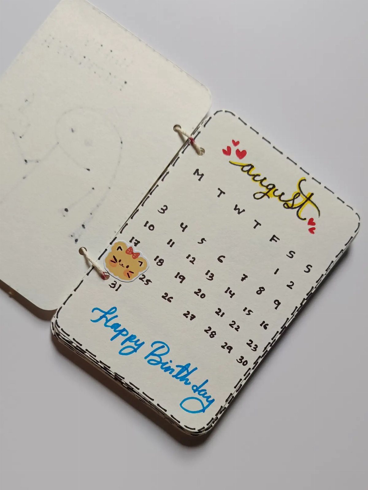 Handmade August birthday calendar with a cute cat drawing and blue cursive lettering.
