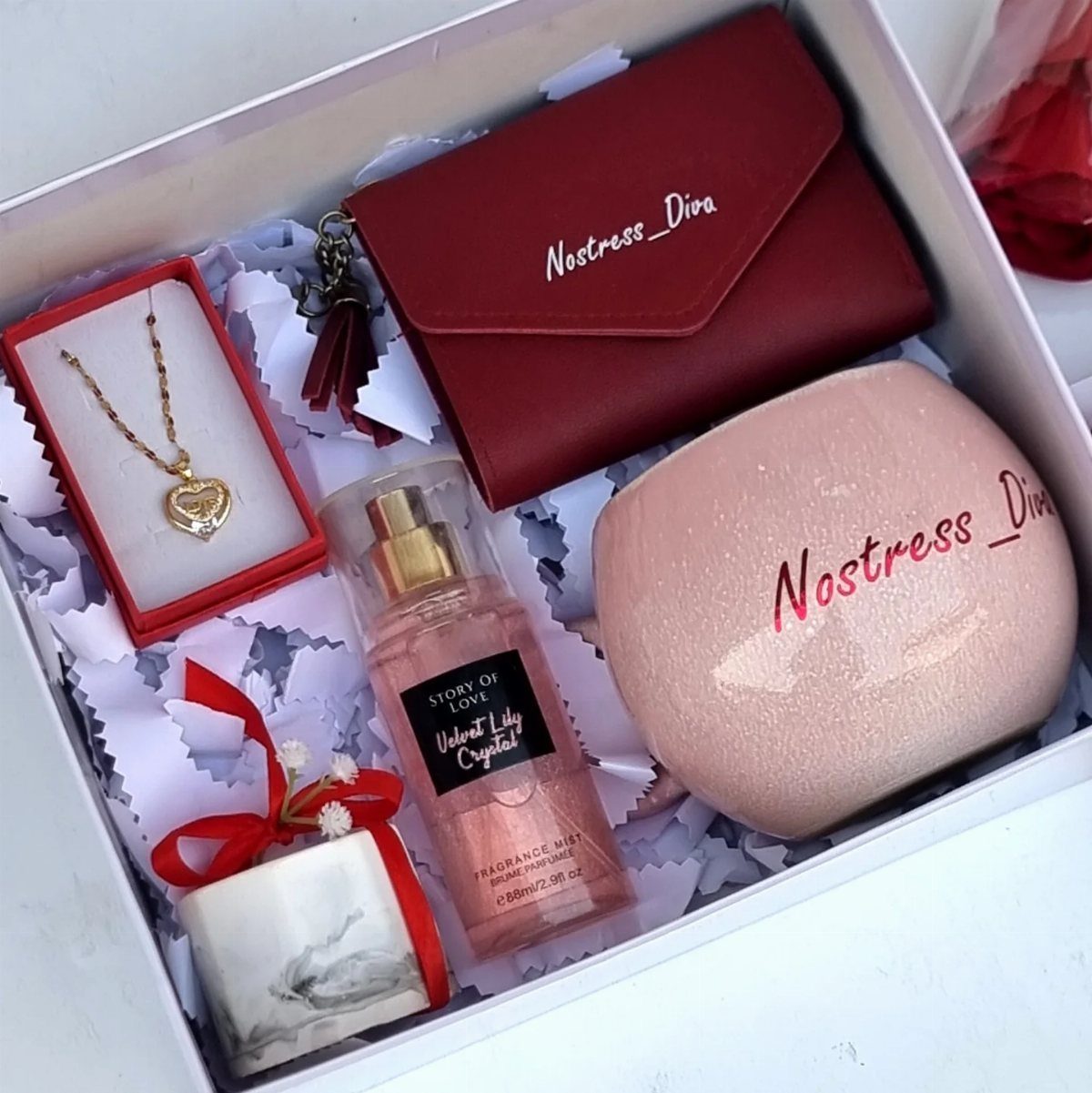 Gift box containing a red wallet, pink pouch, heart necklace, perfume, and candle.