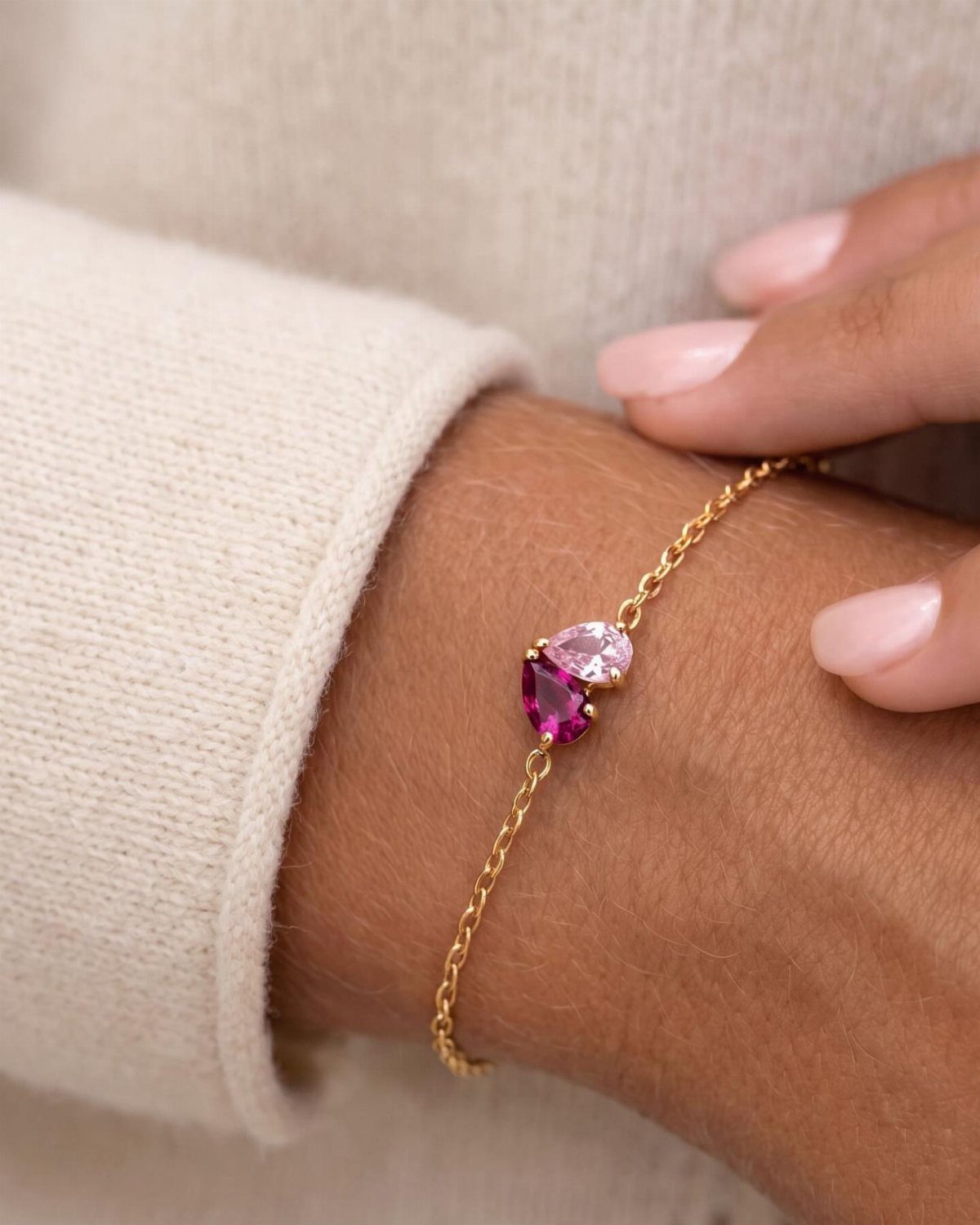 Gold chain bracelet with pink and magenta gemstones on a person's wrist