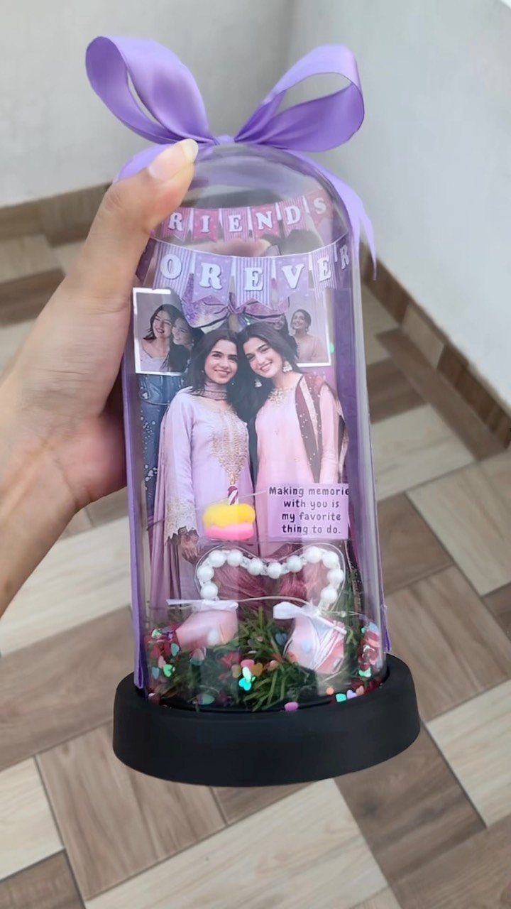 Glass dome display containing photos of two friends, a heart, and purple ribbon.