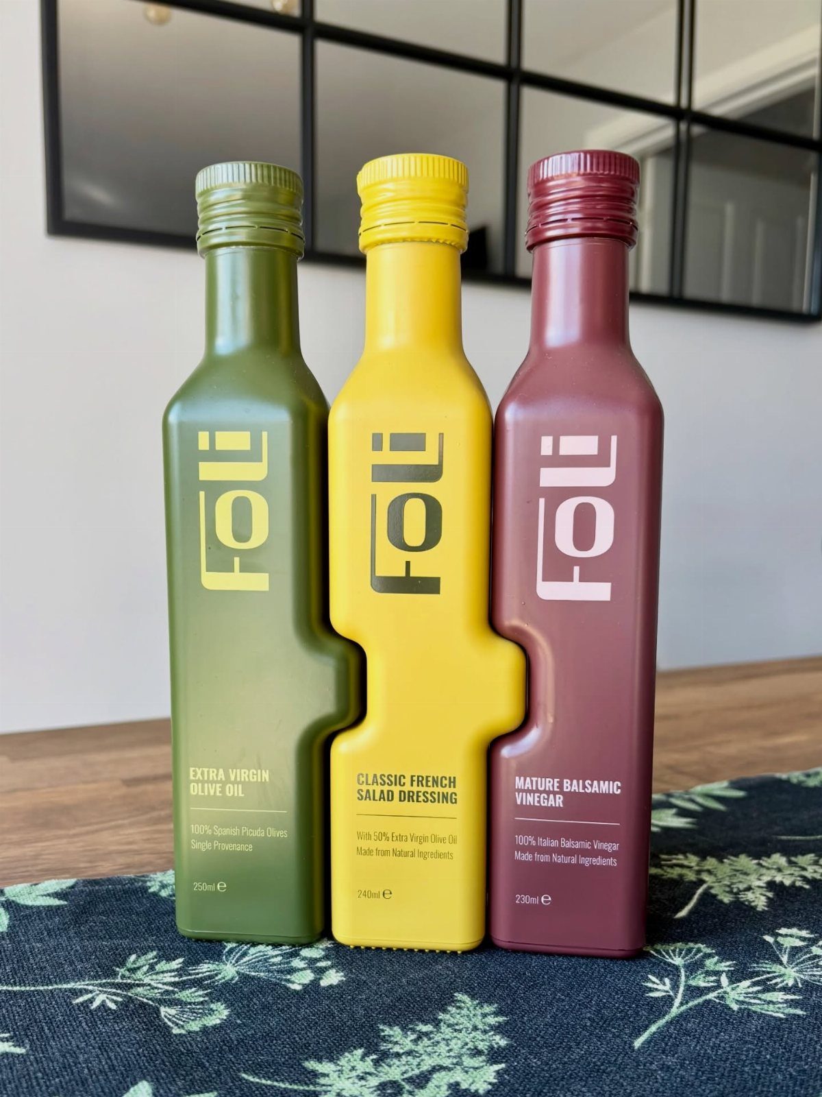 Three matte bottles of olive oil, salad dressing, and balsamic vinegar on wood.