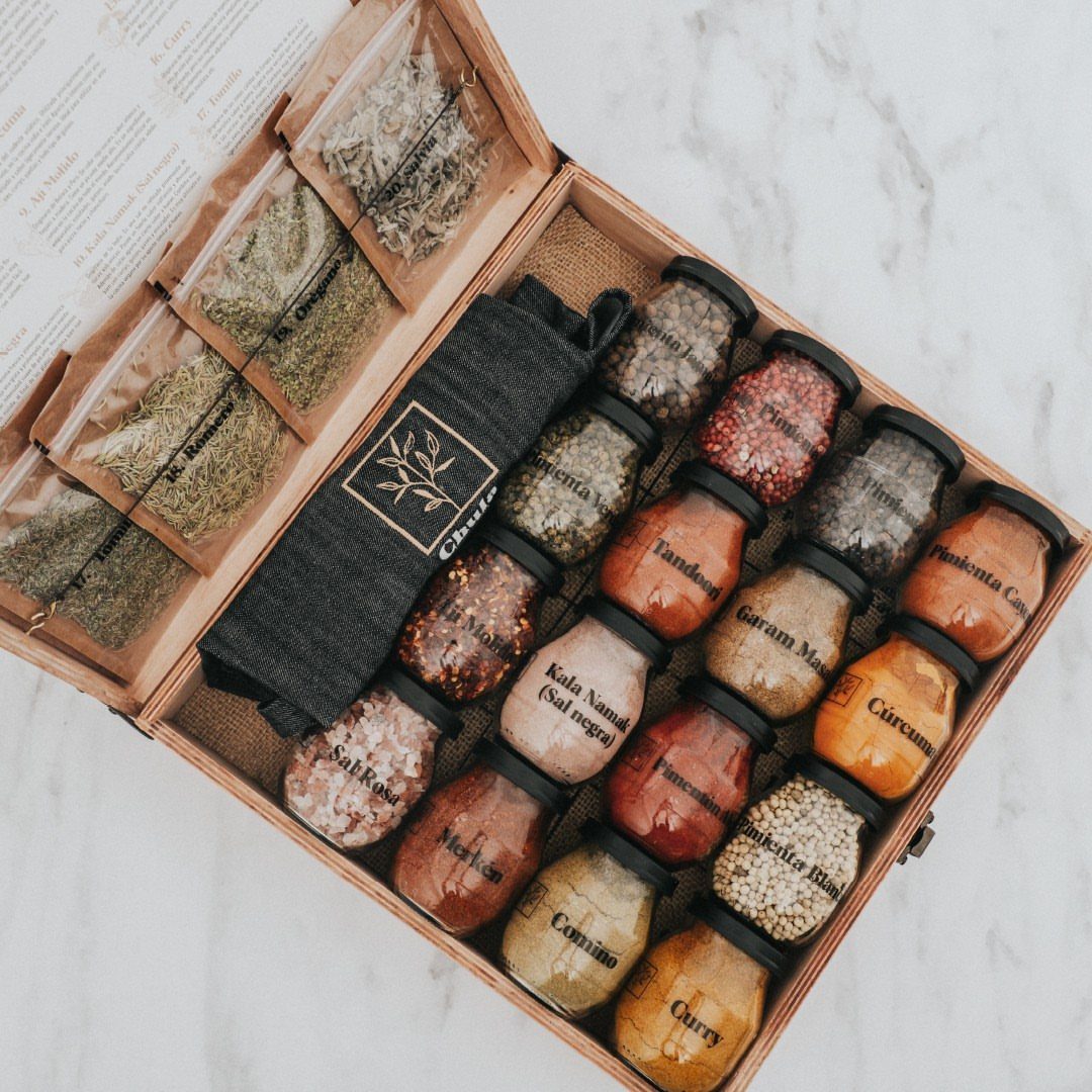 Wooden gift box filled with labeled glass jars of colorful gourmet spices and herbs.