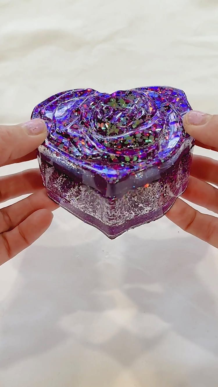 Heart-shaped purple resin container with a glittery rose top held by two hands.