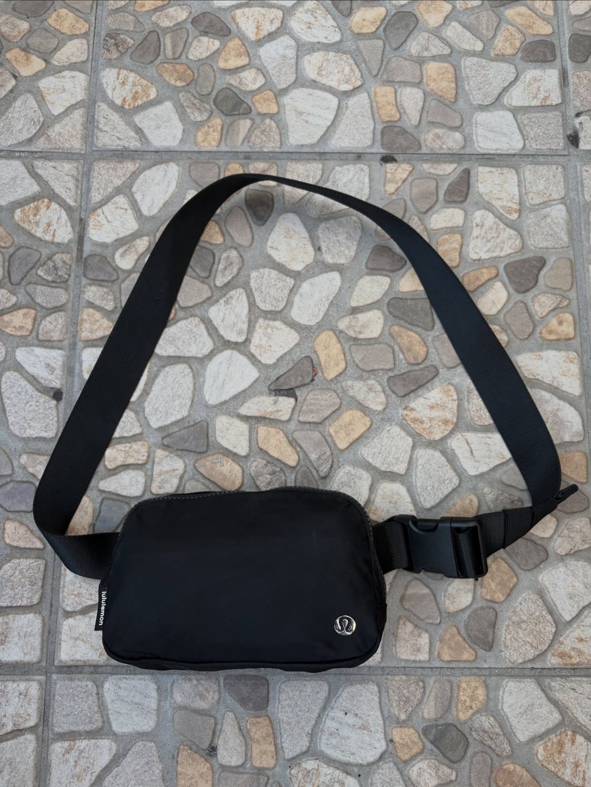 Black lululemon Everywhere Belt Bag resting on a stone tiled surface.