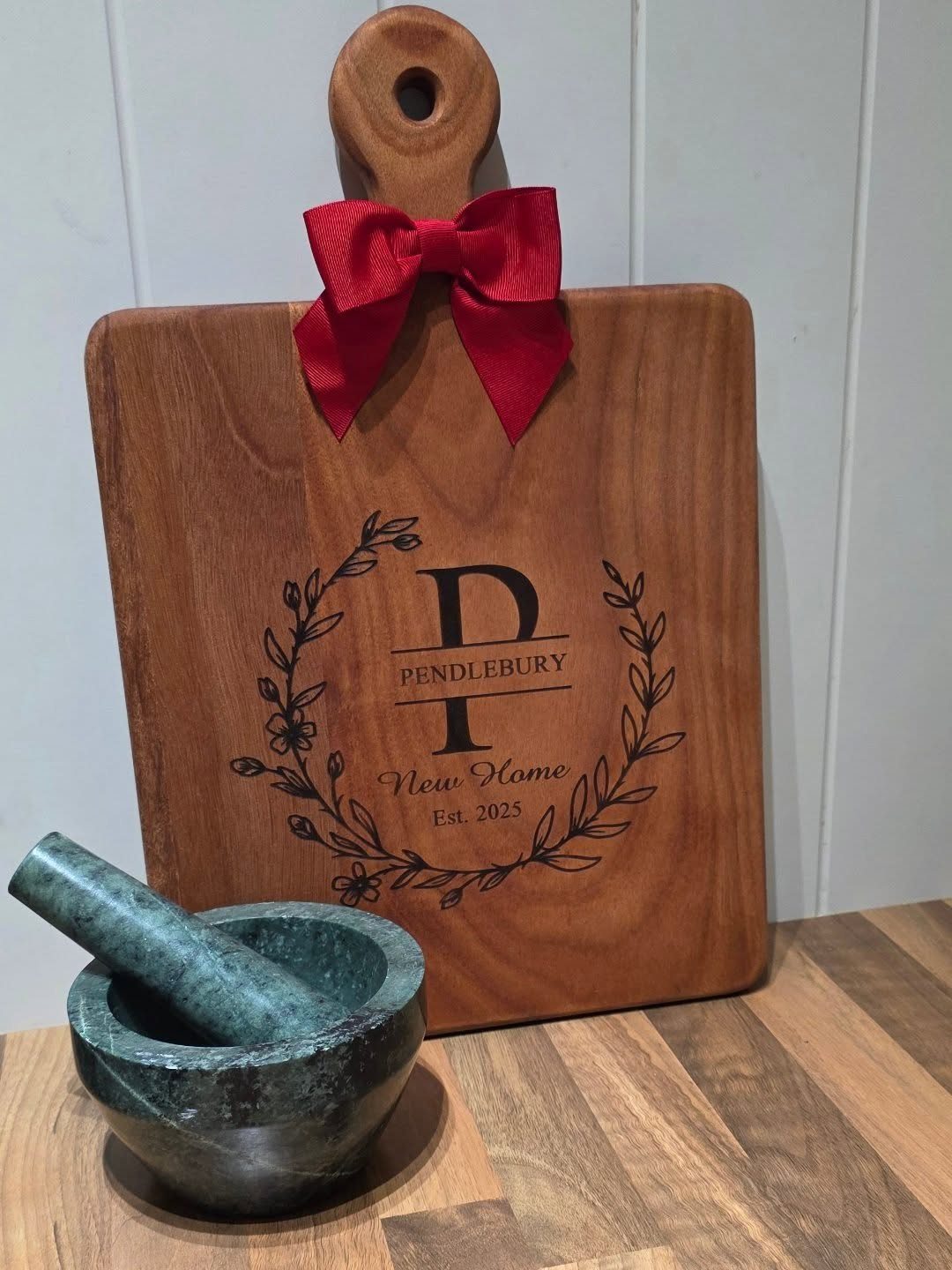 Personalized wooden cutting board with engraved monogram and red bow next to mortar pestle