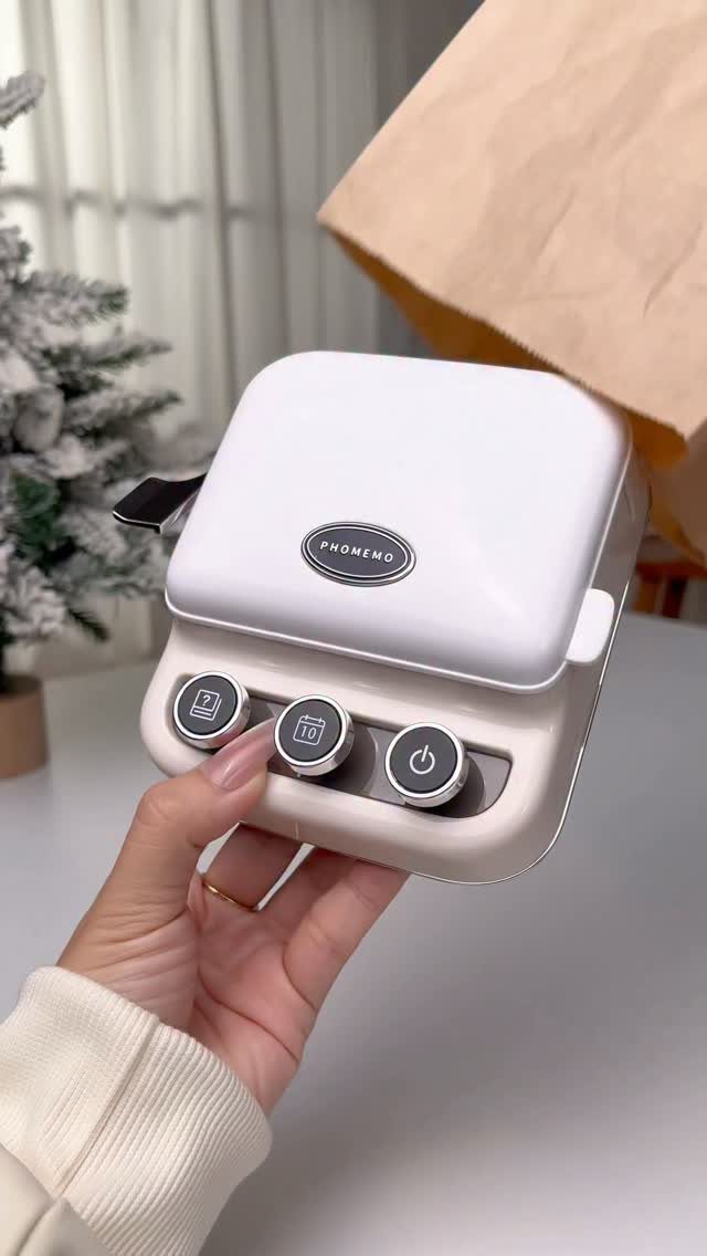 White Phomemo thermal label printer held by a hand against a neutral background