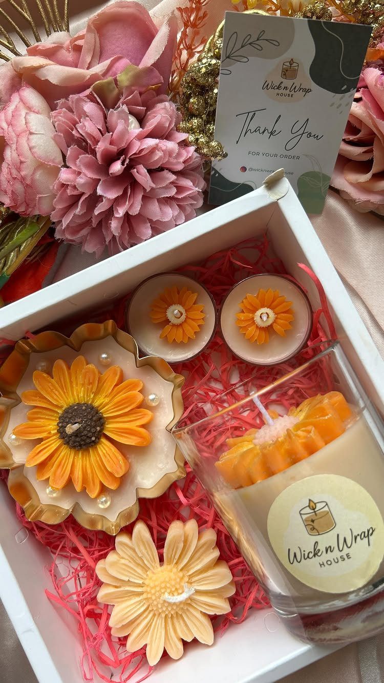 Sunflower-shaped candles and a jar candle in a white gift box with flowers.