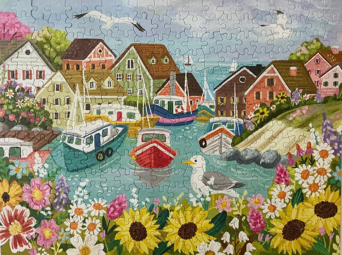 Completed jigsaw puzzle of a colorful coastal village with boats and sunflowers.