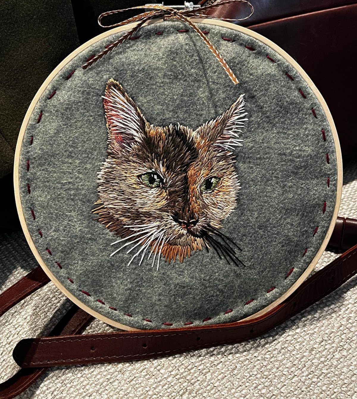 Embroidered tabby cat portrait on grey felt inside a wooden embroidery hoop.