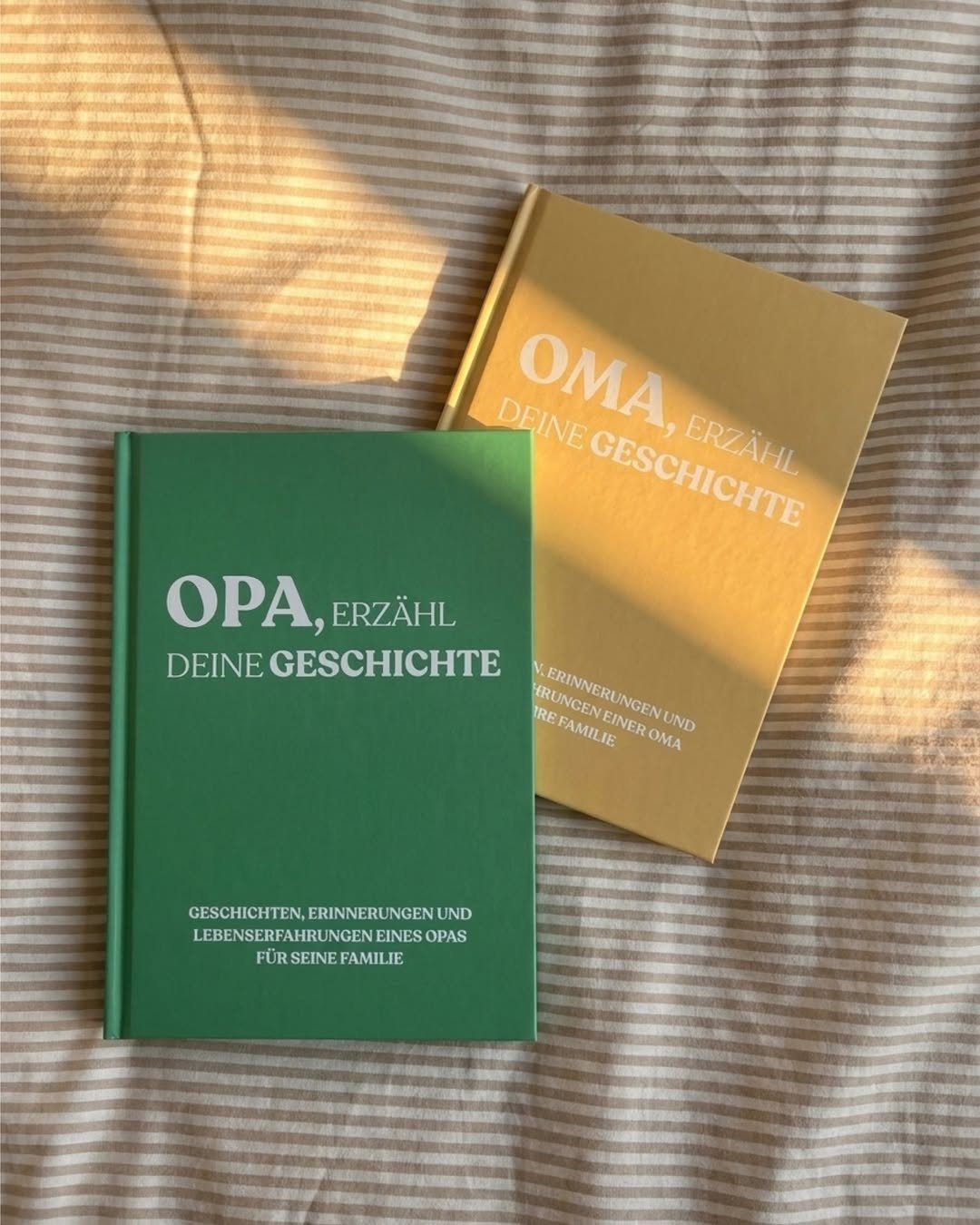 Two hardcover memory journals for grandparents resting on a striped fabric surface.