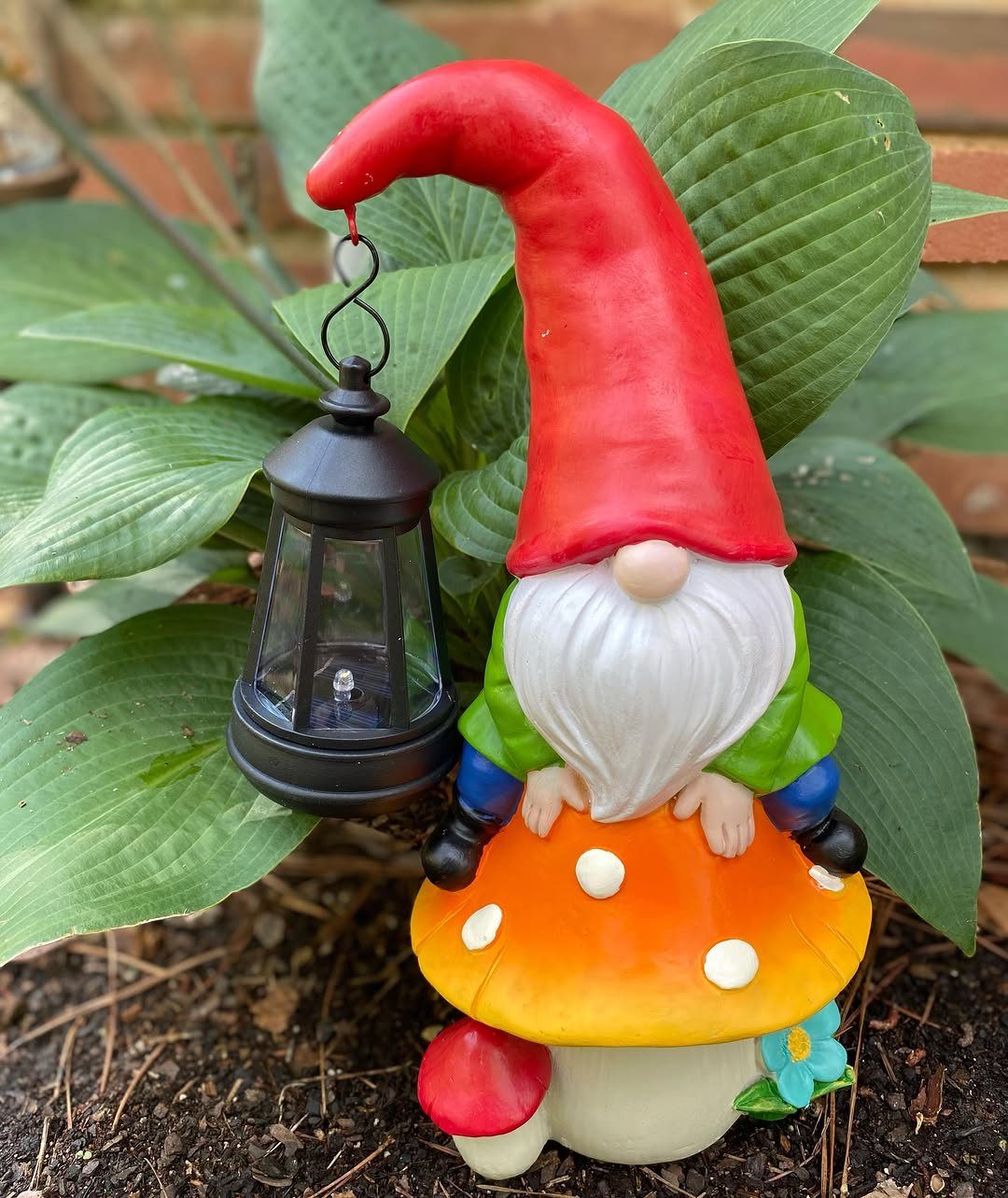Garden gnome with a red hat sitting on a mushroom holding a lantern.