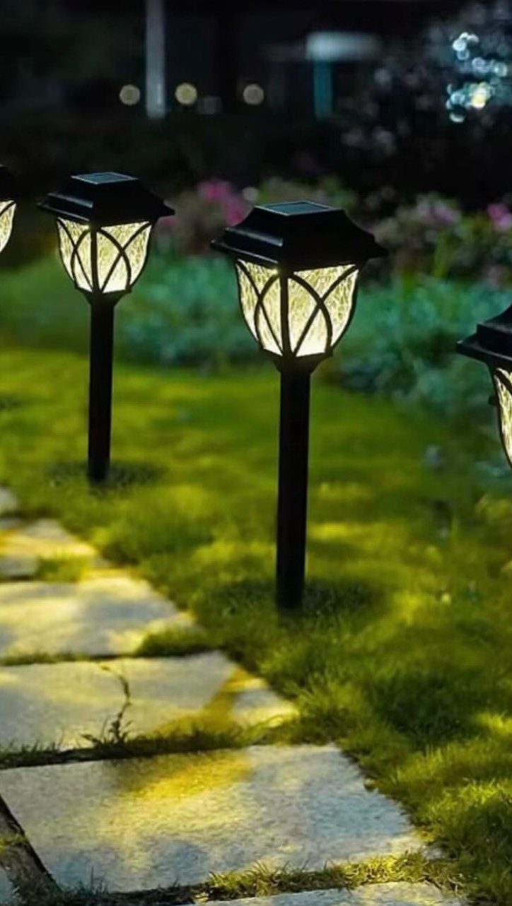 Solar garden stake lights illuminating a stone path in a green yard at dusk.