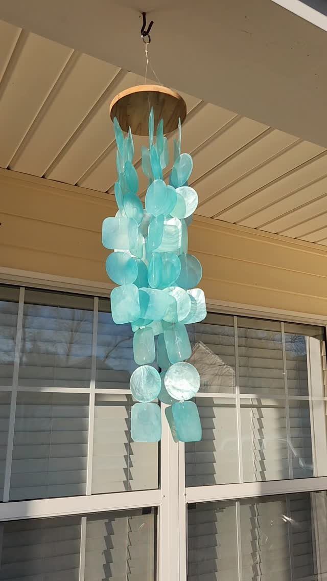 Light blue glass wind chimes hanging from a beige porch ceiling.