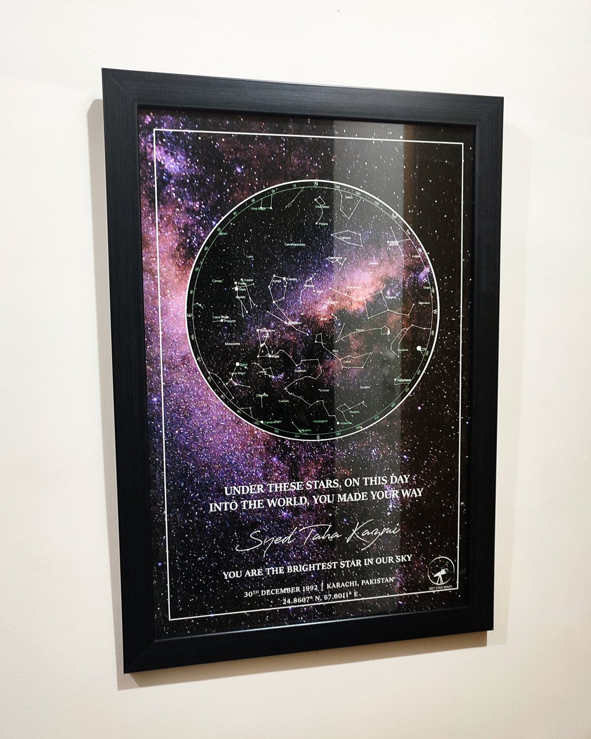 Framed custom star map with purple nebula and personalized text on white wall