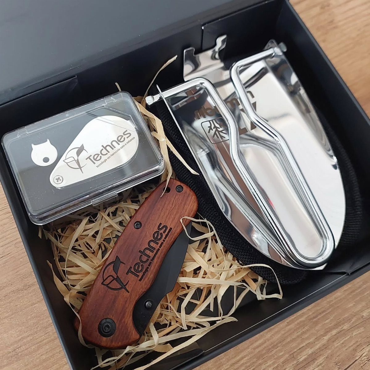 Gift box with a wooden folding knife and silver multi-tool on shredded paper.