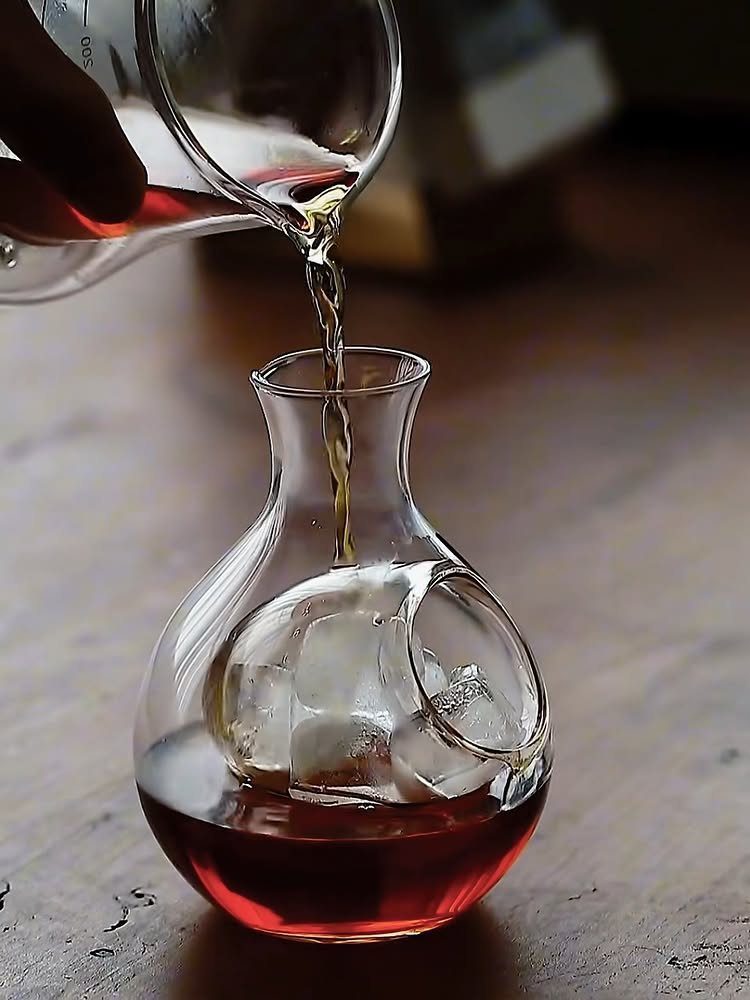 Glass decanter with internal ice chamber being filled with amber whiskey liquid.